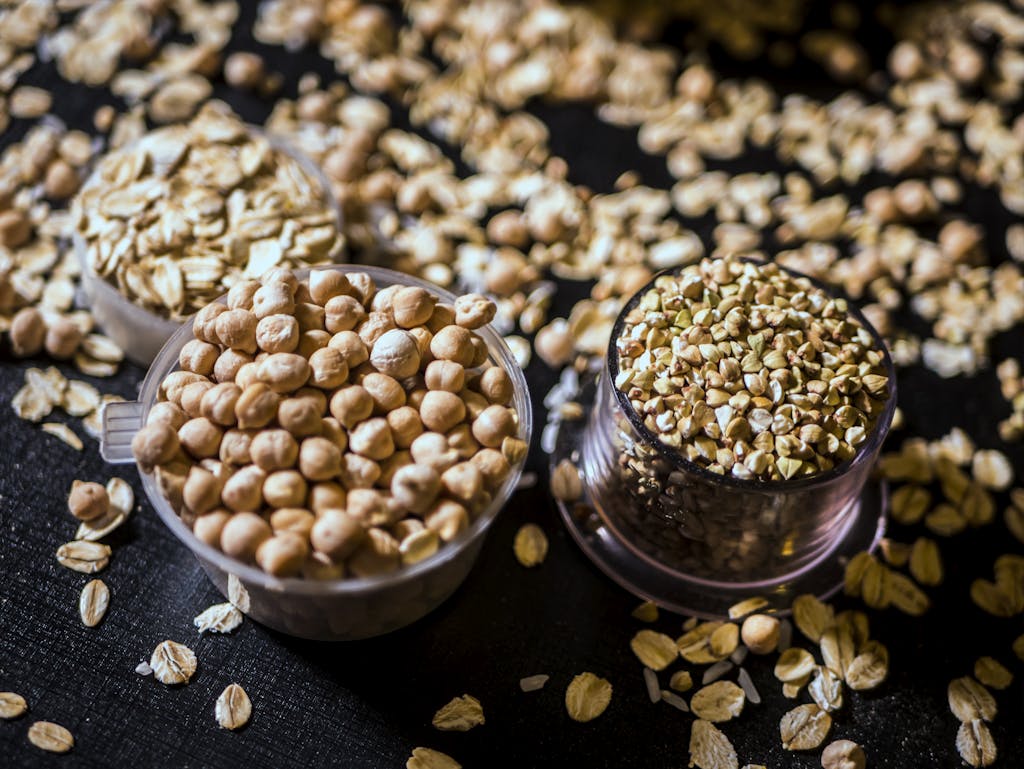 Close-up of assorted raw grains and seeds in cups on a dark background, showcasing variety and texture.